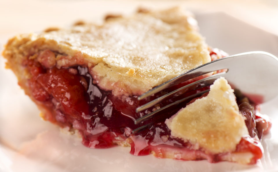 Up close of a slice of cherry pie being cut with a fork.