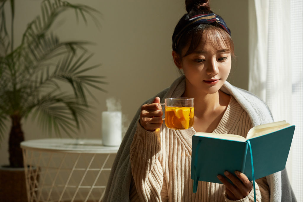 A young woman sipping tea and reading a book