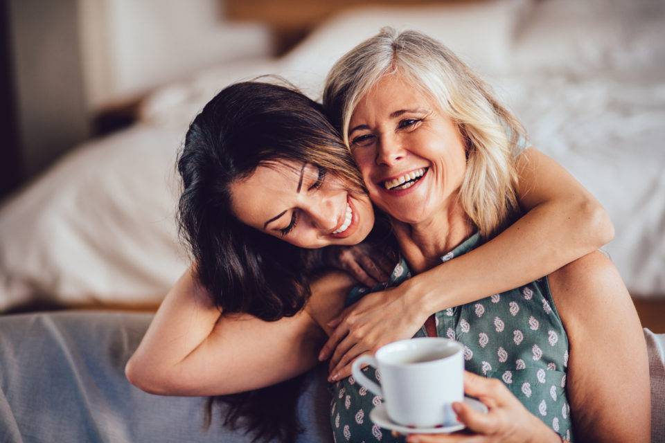 Loving adult daughter embracing cheerful senior mother at home
